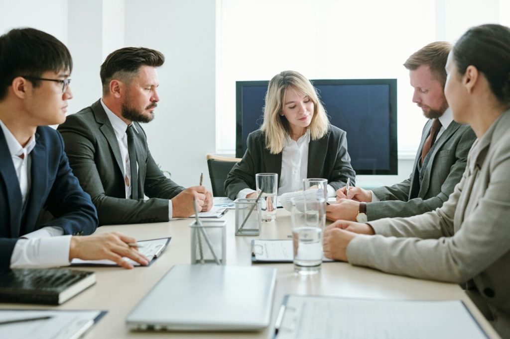 Confident young blond female coach in formalwear sitting in front of audience